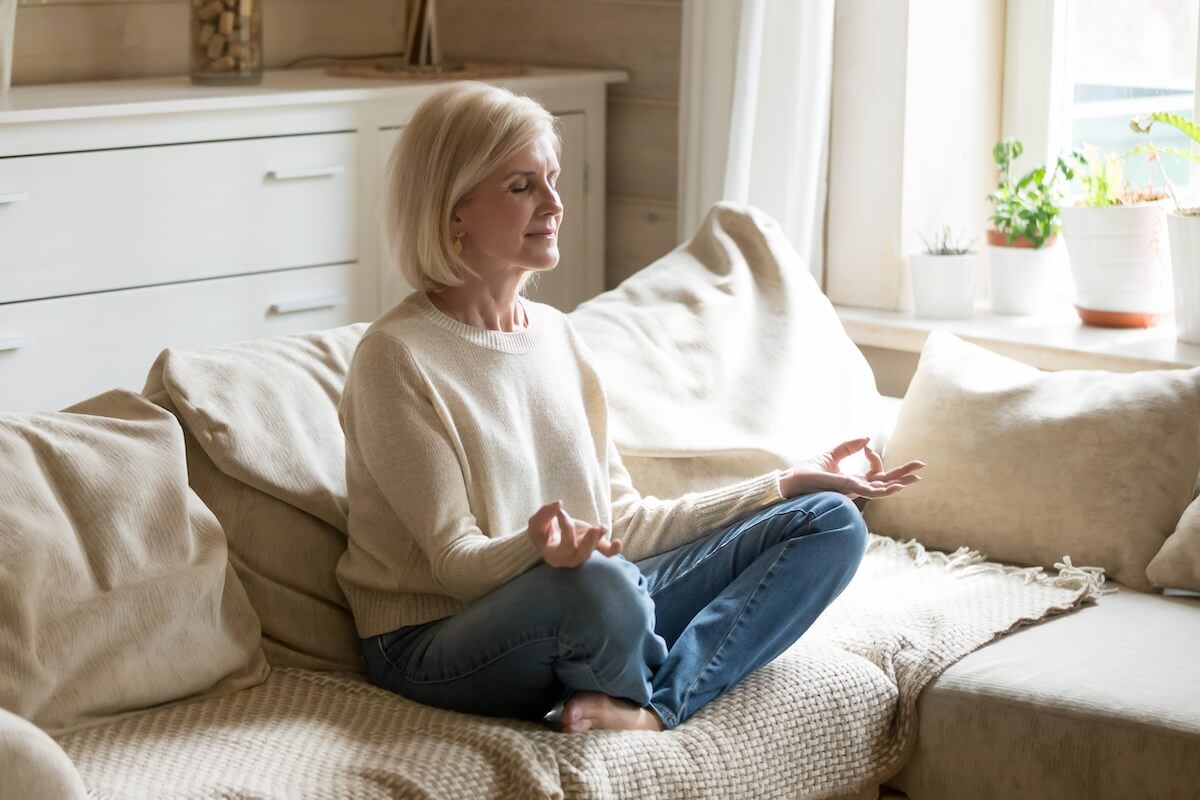 Mindful ways to practice self care mature woman practicing meditation at home, calm senior middle aged lady sitting on couch in lotus pose doing yoga for mental balance breathing air relaxing on stress free weekend