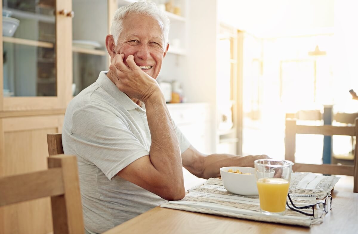 Senior, man and happy with portrait at breakfast in dining room for nutrition. healthy meal and retirement. Elderly, person and smile in home with porridge, relax and morning routine in apartment Senior Daily Routine Tips